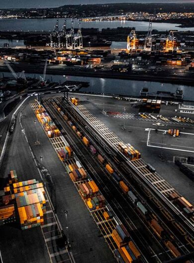 Golden hour photo of the New Jersey Dockyard in Upper Bay, New York City. Numerous cranes, gantries and shipping containers lit with street lights. Taken from a helicopter.